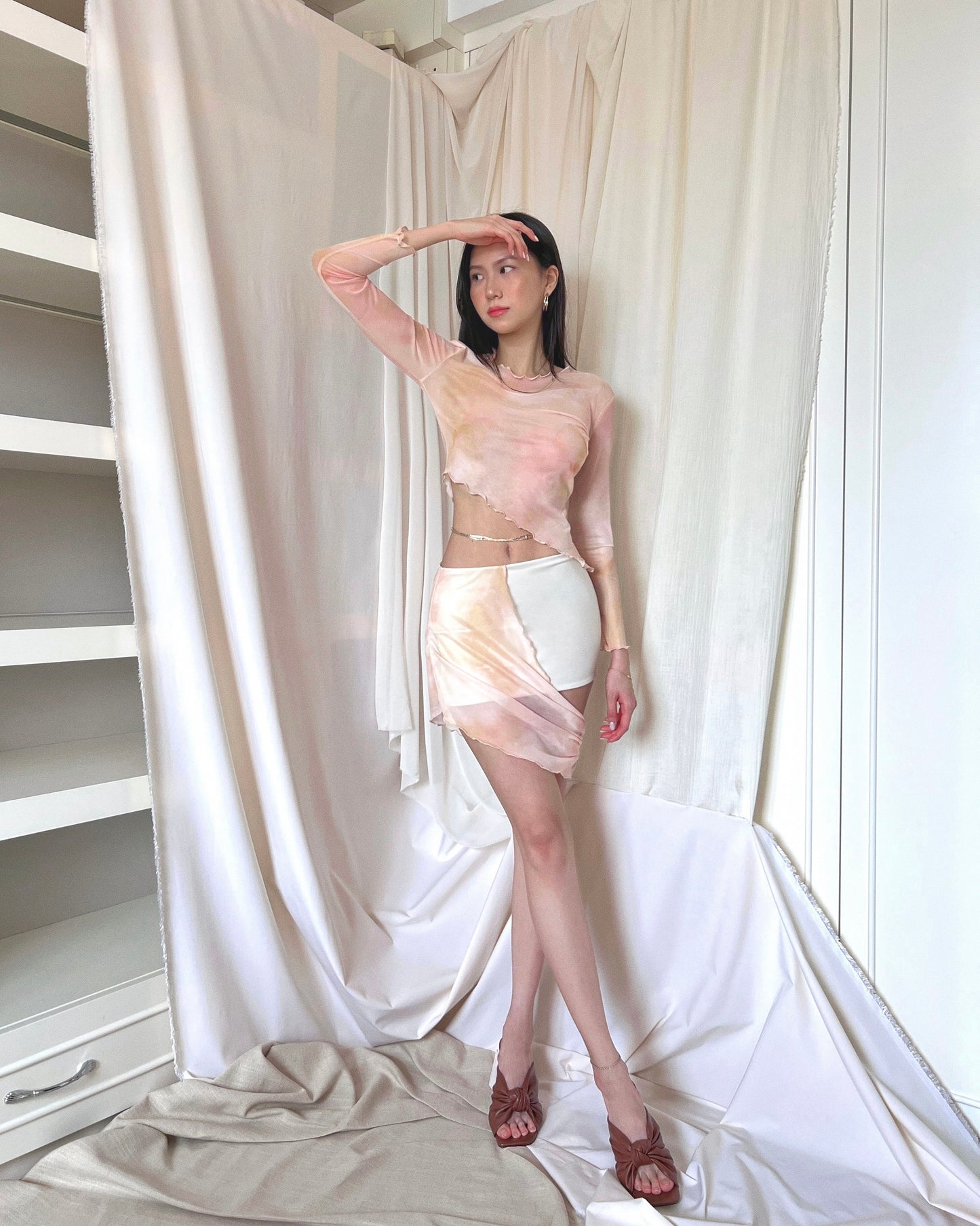 An asymmetrical sunset orange printed mini skirt in nylon fabric and mesh panel. Styled with an asymmetrical sunset orange printed long sleeve mesh top and brown mules.