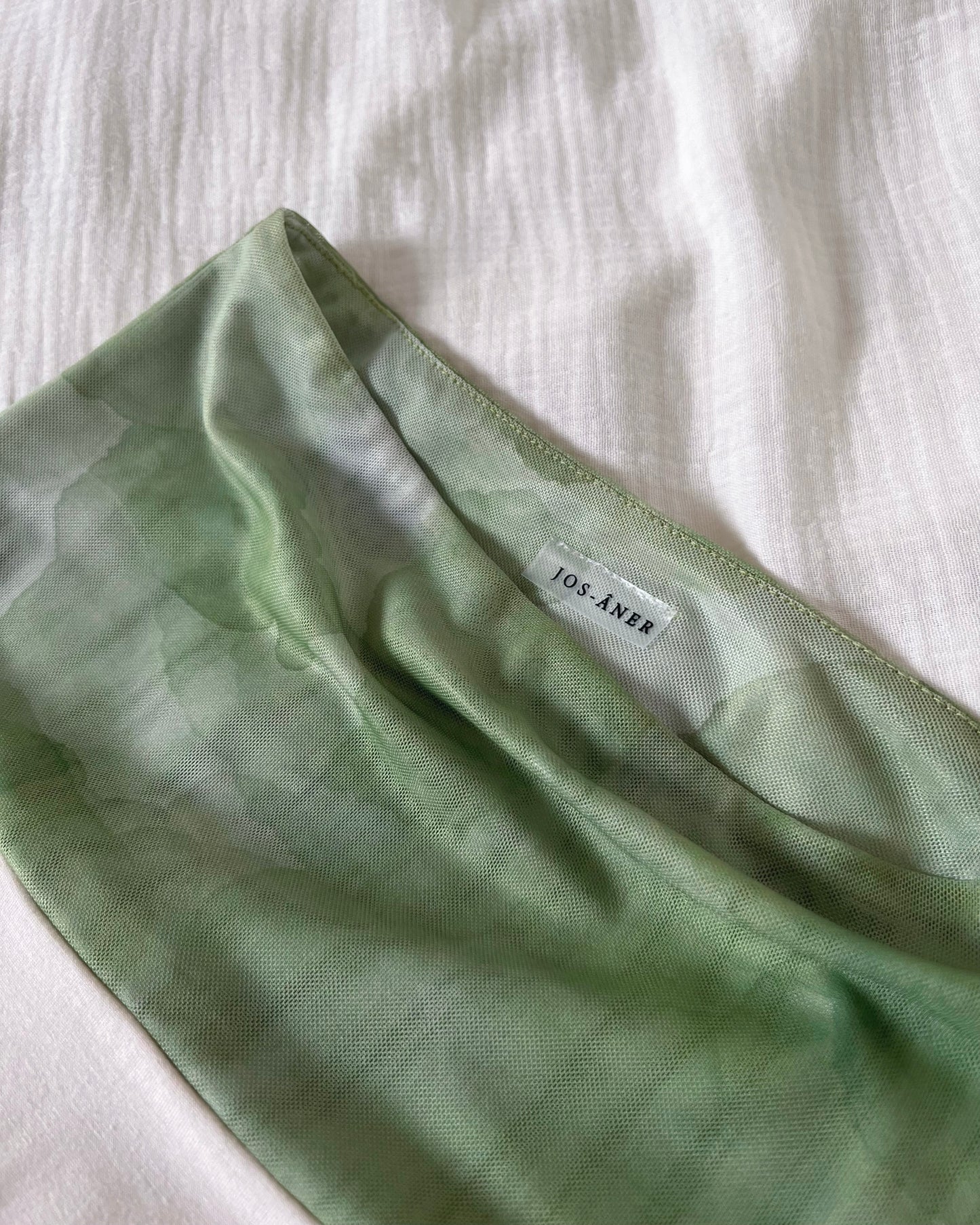 An asymmetrical matcha green modal midi skirt with printed sheer bottom panel and printed sheer wide waistband.