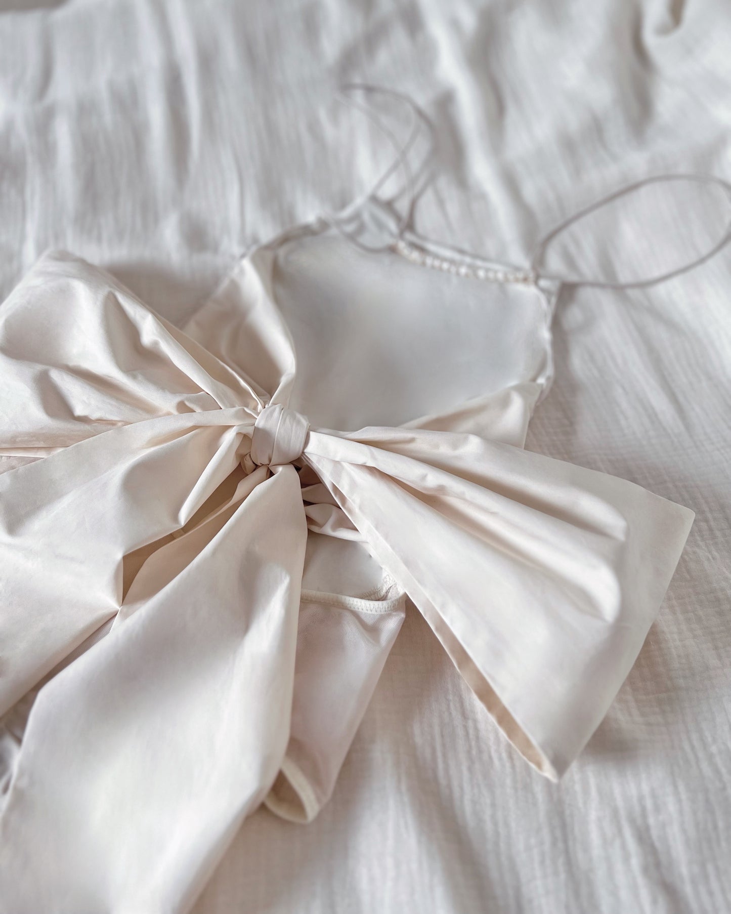 Formfitting ivory bodysuit, made in smooth and soft nylon fabric, with side mesh panels and wide and long woven back straps as bow.
