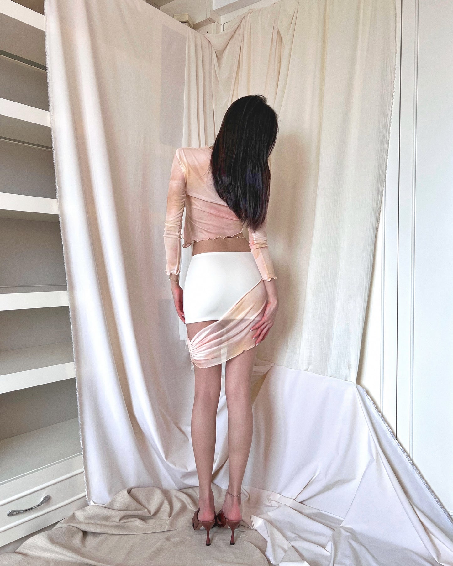 An asymmetrical sunset orange printed mini skirt in nylon fabric and mesh panel. Styled with an asymmetrical sunset orange printed long sleeve mesh top and brown mules.