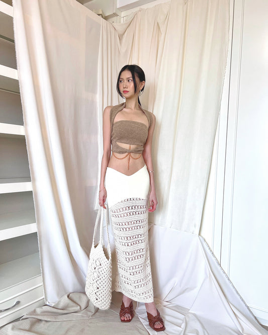 Strapless brown knit top with front twisted knot, long back straps and semi-iridescent beads around waist. Styled with a crochet maxi skirt, brown mules and a crochet tote bag.