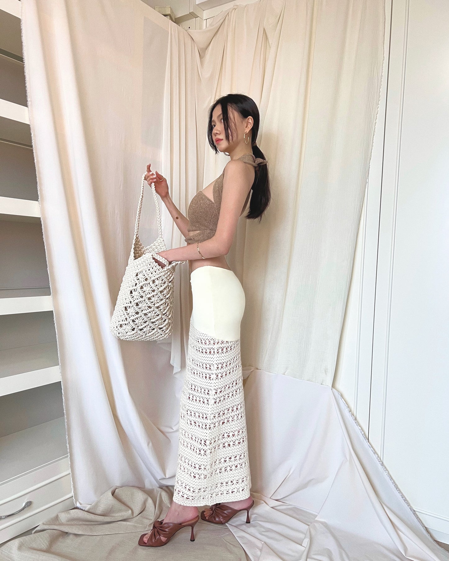 Strapless brown knit top with front twisted knot, long back straps and semi-iridescent beads around waist. Styled with a crochet maxi skirt, brown mules and a crochet tote bag.