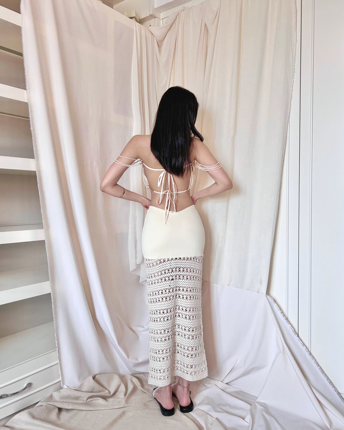 A freshwater pearl embellished sleeveless white knit top with back thin woven straps. Styled with an ivory crochet maxi skirt with nylon fabric and crochet fabric and a symmetrically diagonal waistline and pearl slides.