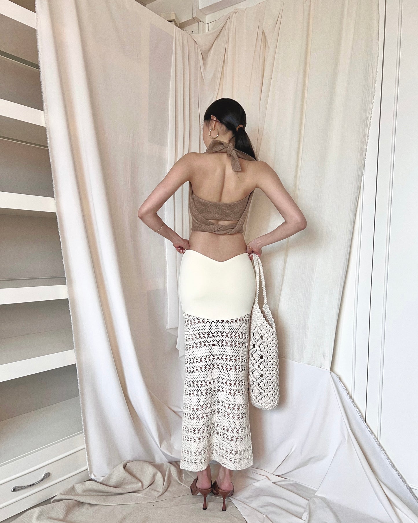 Strapless brown knit top with front twisted knot, long back straps and semi-iridescent beads around waist. Styled with a crochet maxi skirt, brown mules and a crochet tote bag.