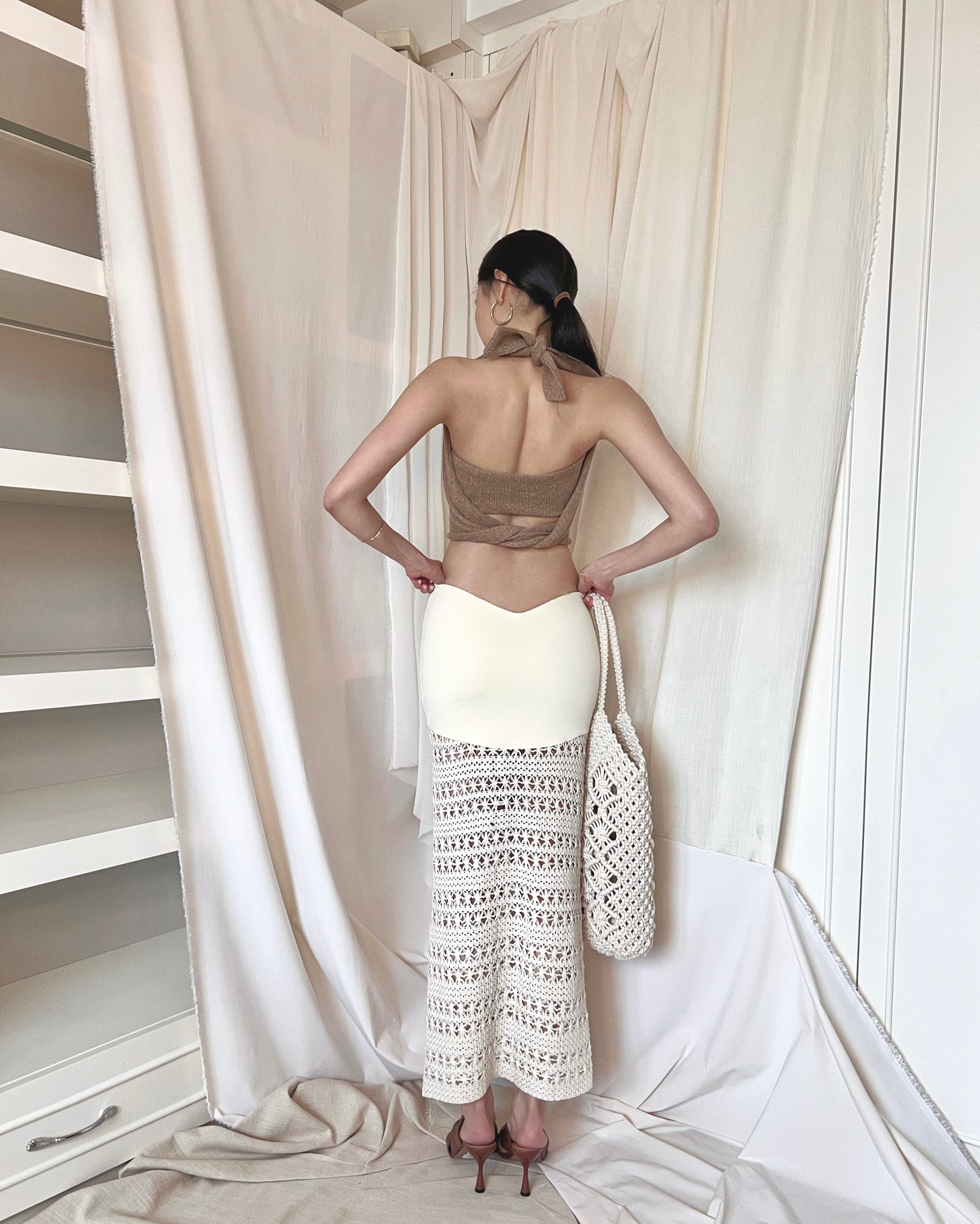 Strapless brown knit top with front twisted knot, long back straps and semi-iridescent beads around waist. Styled with a crochet maxi skirt, brown mules and a crochet tote bag.