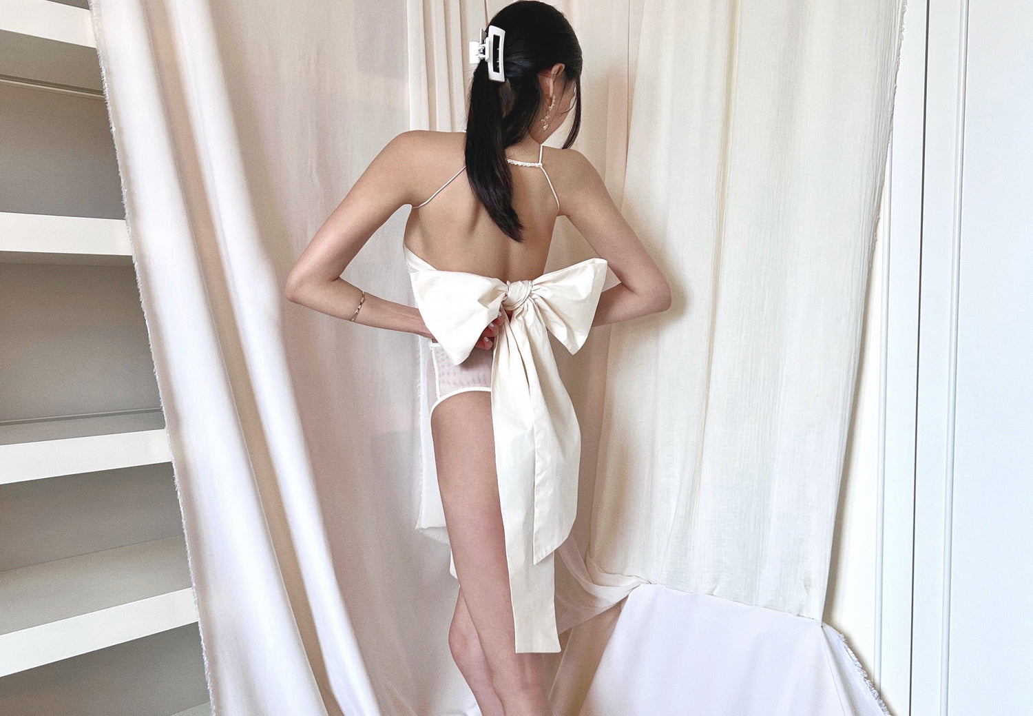 Formfitting ivory bodysuit, made in smooth and soft nylon fabric, with side mesh panels and wide and long woven back straps as bow.