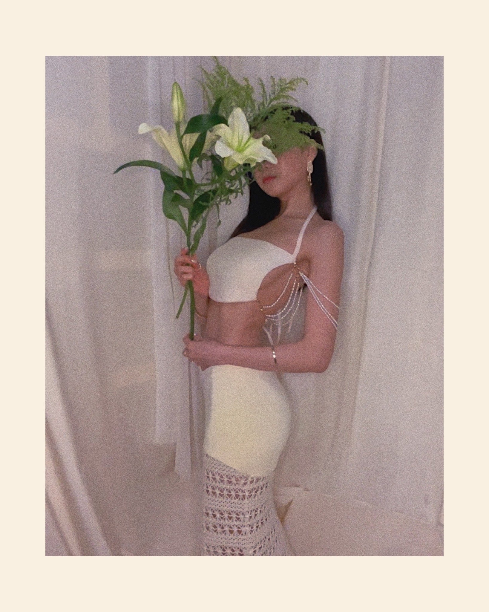 An ivory crochet maxi skirt with nylon fabric and crochet fabric and a symmetrically diagonal waistline. Styled with freshwater pearl embellished sleeveless white knit top.